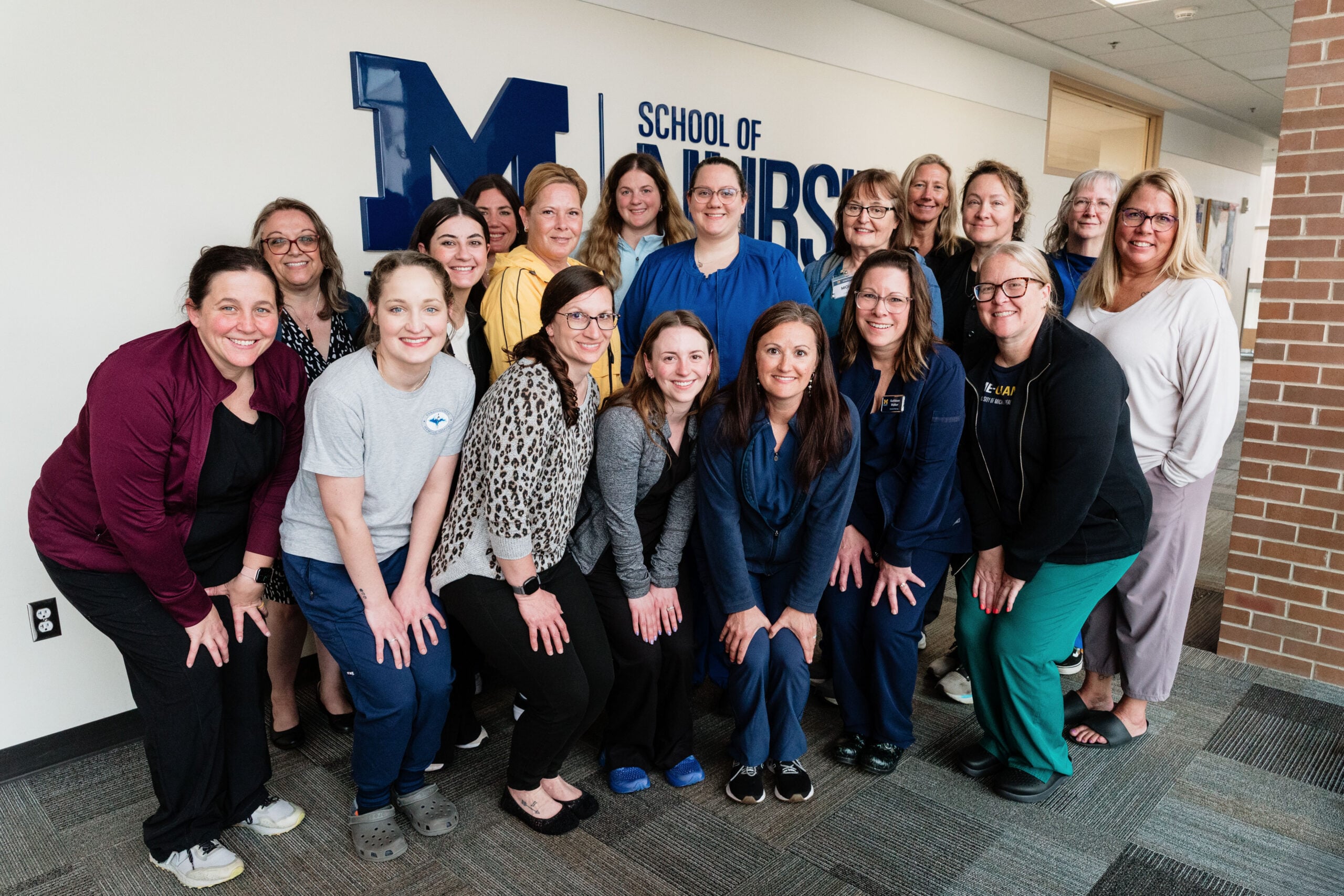 Students from the three-day Pediatric/Adolescent SANE Boot Camp gather in front of a white wall in the William S. White Building with the UM-Flint School of Nursing logo