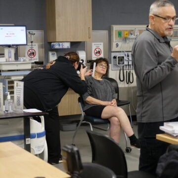 Photographer Eric Johnson instructs students about forensic photography techniques, while in the background, a SANE student practices taking images of physical evidence with the help of a standardized patient