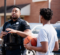 A police officer in a black uniform talks to a young person holding a basketball in a residential area.