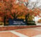 Sign for the University of Michigan-Flint, surrounded by autumn foliage, with a brick pathway in the foreground.