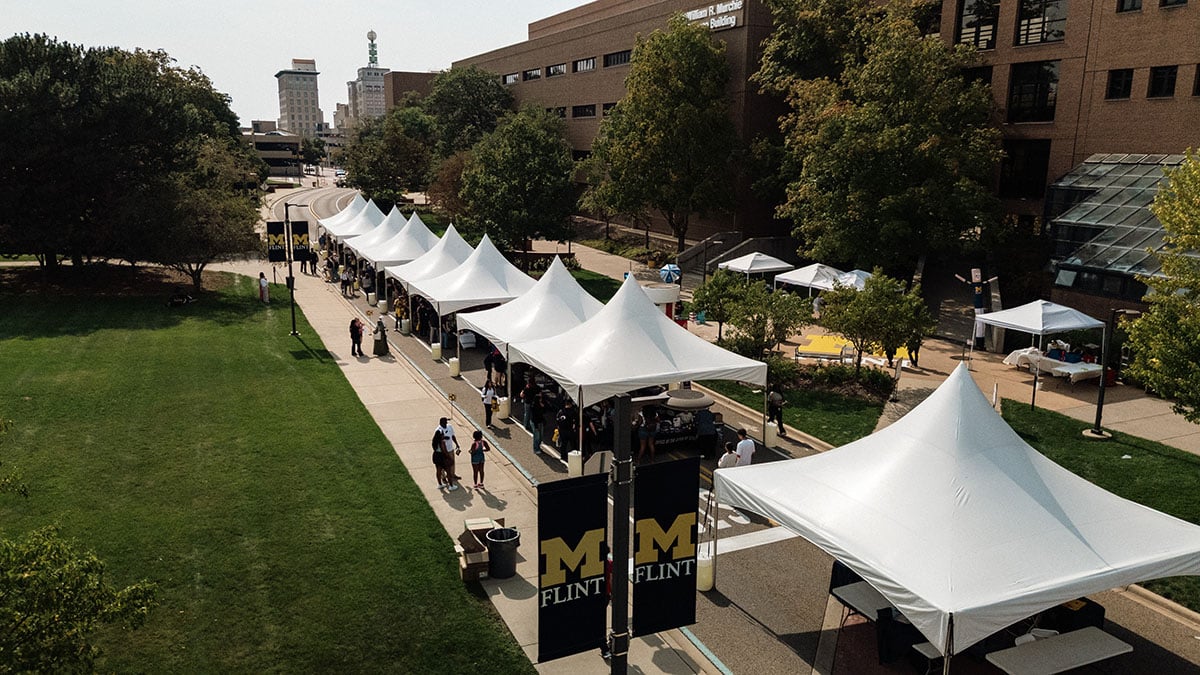 default Aerial view of a university campus with several white tents set up along a pathway, surrounded by greenery and buildings.