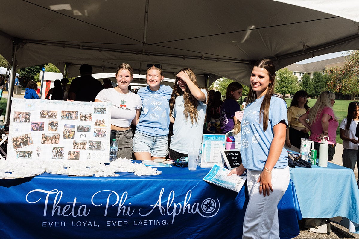 FLINT_M'Gagement Fair 2026_0030 A group of four young women at a booth for Theta Phi Alpha, showcasing a display board with photos and information about the organization.