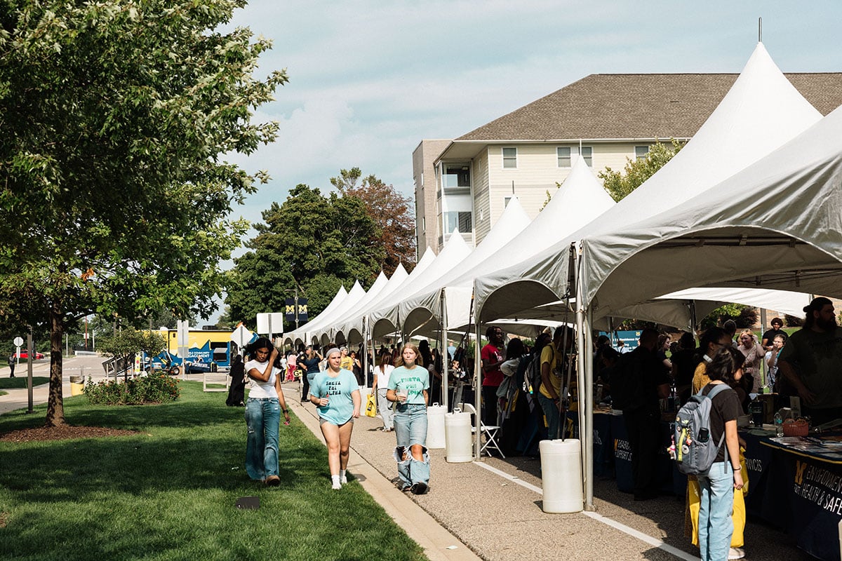 FLINT_M'Gagement Fair 2026_0037 A lively outdoor event with several large white tents lined up, people walking along a path, and attendees engaging at booths.
