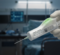 A gloved hand holding a syringe with a digital display, set in a medical environment with equipment in the background.