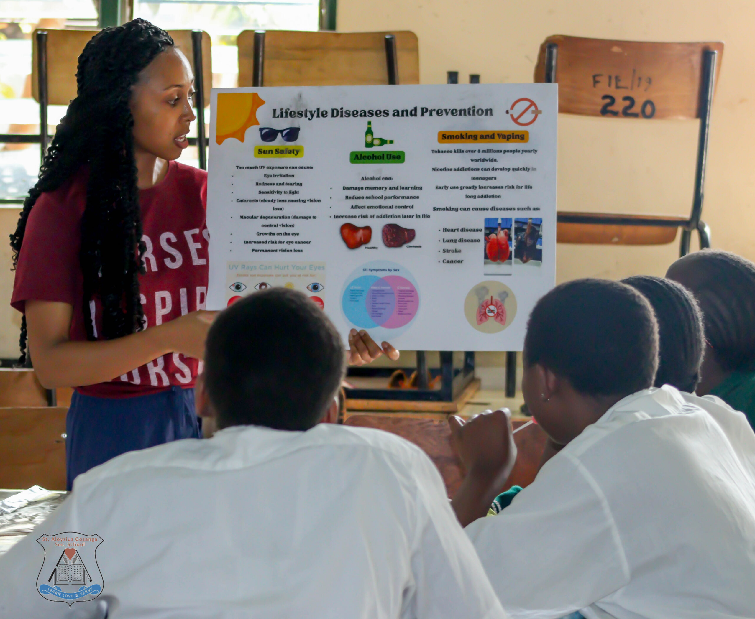 A woman is presenting a poster titled "Lifestyle Diseases and Prevention" to a group of seated individuals. The poster includes information on sun safety, alcohol use, and smoking and vaping, highlighting health risks and prevention methods.